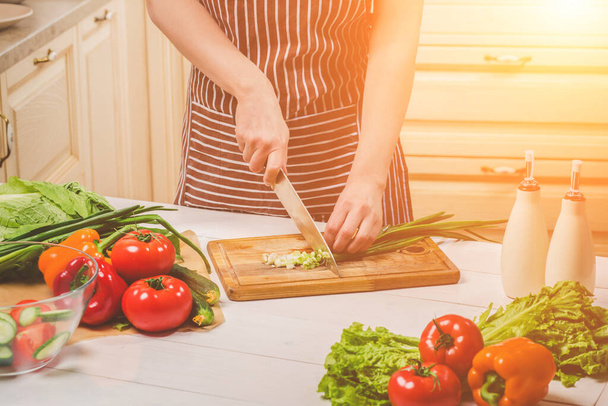 Young woman cooking in the kitchen at home. Healthy food. Diet. Dieting concept. Healthy lifestyle. Cooking at home. Prepare food. A woman cuts a green onion and vegetables with a knife. - Photo, Image