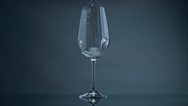 Water pouring wine glass at dark background closeup. Clear liquid splashing in beautiful transparent jug. Mineral fluid fill flowing into glassware. Refreshing drink beverage healthy lifestyle concept - Felvétel, videó