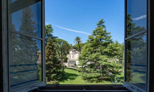 Вигляд через відчинене вікно одного з музеїв Ватикану (Рим) на гарні сади й будівлі. - Фото, зображення