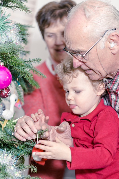 クリスマス ツリーを飾る孫と祖父母 - 写真・画像