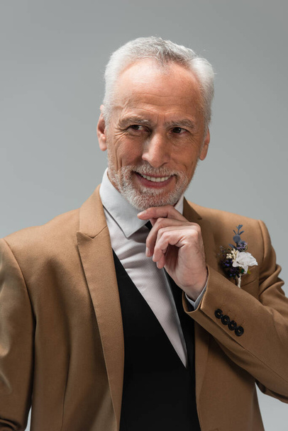 cheerful middle aged groom in suit with floral boutonniere isolated on grey  - Fotó, kép