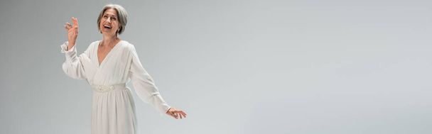 amazed middle aged bride in white wedding dress gesturing isolated on grey, banner - Fotoğraf, Görsel