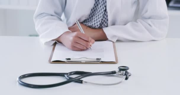 Doctor filling out health insurance paperwork, while sitting at a desk. A male general practitioner writing a prescription on a clipboard. Physician adds notes to a patients medical chart, closeup. - Filmagem, Vídeo