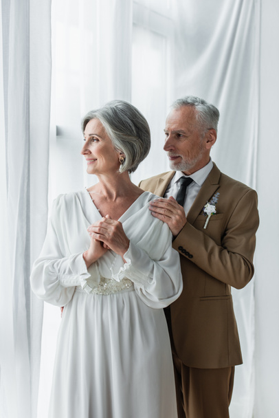 bearded middle aged groom in suit touching shoulder of happy bride in white dress - Fotoğraf, Görsel