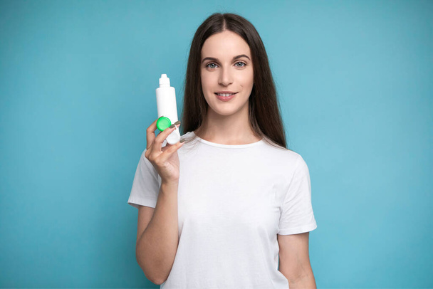 Young woman with contact lenses and bottle of solution on color background. High quality photo - Φωτογραφία, εικόνα