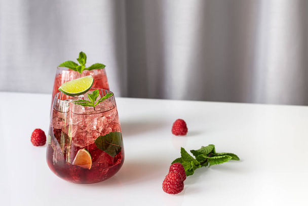 Fresh summer lemonade with raspberry, lime, soda water, and ice in glasses. Cold refreshing drink, cocktail or mocktail. - Foto, Bild
