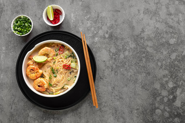 Bowl of curry laksa, a spicy glass noodle dish popular in Southeast Asia with prawns, bok choy, lime, ginger, and chili. Most variations of laksa are prepared with a rich and spicy coconut soup. - Fotó, kép