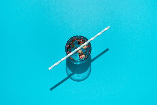 Drink in glass with dried roses, red peppers and striped paper straw on blue background. - Foto, Imagem
