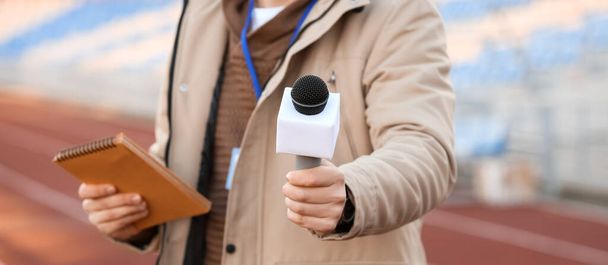 Мужчина-репортер с микрофоном на стадионе, крупный план
 - Фото, изображение