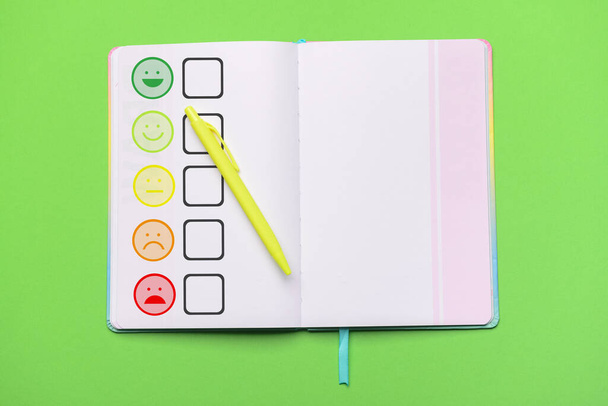 Блокнот з рейтингом задоволення та ручкою на зеленому фоні
 - Фото, зображення