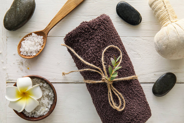 Composition with clean towel, sea salt, spa stones and massage bag on light wooden background - Foto, afbeelding