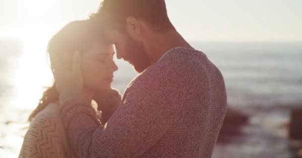Ρομαντικό, ερωτευμένο και αγκαλιασμένο νεαρό ζευγάρι που μοιράζεται μια τρυφερή γλυκιά στιγμή, περνώντας ποιοτικό χρόνο και δένοντας σε μια παραλία κατά τη διάρκεια ενός ηλιοβασιλέματος με φωτοβολίδα. Ένας άντρας και μια γυναίκα σε ένα χαλαρωτικό ραντεβού δίπλα στον ωκεανό.. - Πλάνα, βίντεο