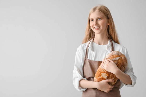 Young woman with fresh bread on light background - Foto, afbeelding