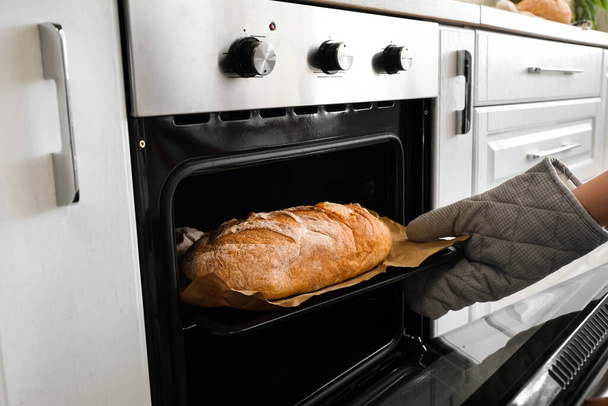 Woman taking baking sheet with bread from oven in kitchen, closeup - Foto, immagini