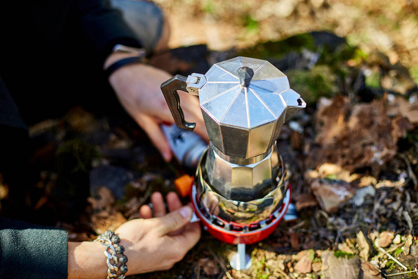 Man brewing coffee from a geyser coffee maker on a gas burner,, autumn outdoor. Male prepares coffee outdoors, travel activity for relaxing, bushcraft, adventure, travel, tourism and camping concept - Zdjęcie, obraz