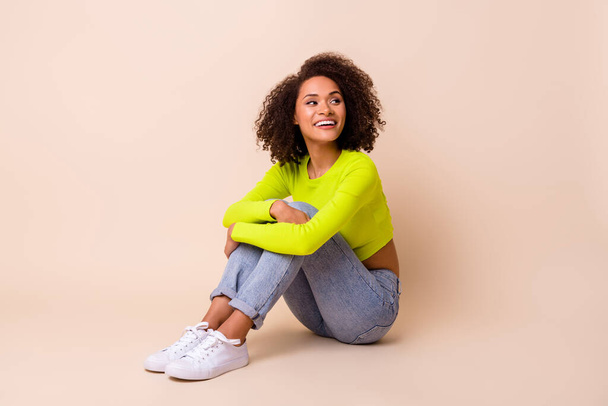 Full size photo of nice young lady curly hair sit embrace knees enjoy rest dressed stylish yellow look isolated on beige color background. - Photo, Image