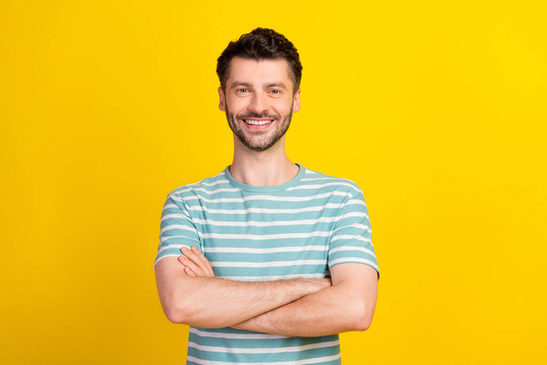Portrait of young attractive man wear blue striped t-shirt hands folded genius influencer looking you isolated on yellow color background. - Foto, Imagem