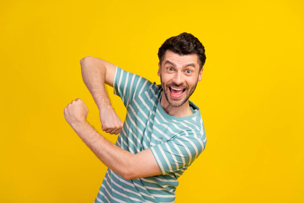 Photo of cheerful handsome guy dressed striped t-shirt dancing rejoice arms fists discount shopping isolated on yellow color background. - Foto, Imagem
