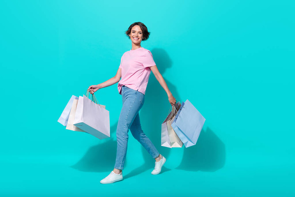 Full length photo of pretty lady wear trendy stylish outfit jeans clothes walk hand arm hold purchase isolated on cyan color background. - Фото, изображение