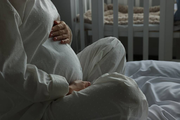 Pregnant woman in pajamas on bed at home, closeup - Foto, afbeelding