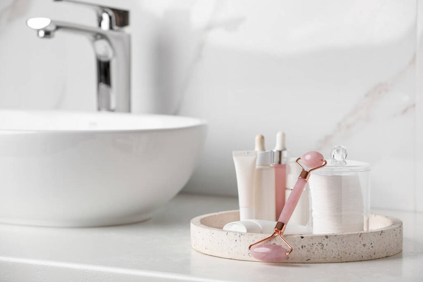 Natural face roller and tray with cosmetic products on counter in bathroom. Space for text - Fotoğraf, Görsel
