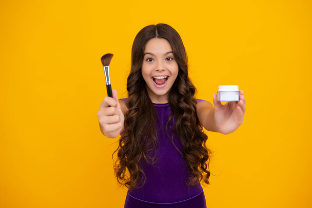 Beauty, make up and kids cosmetics. Teenage girl with brush applying blush to face isolated on yellow studio background. Happy girl face, positive and smiling emotions - Foto, imagen