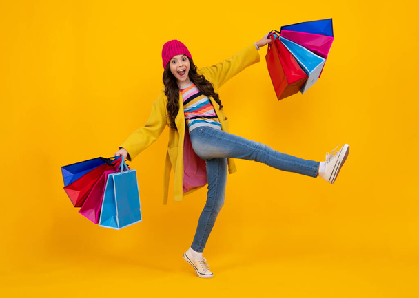 Autumn shopping sale. Teen girl holding shopping bags, isolated on studio background. Run and jump. Happy teenager, positive and smiling emotions of teen girl - Foto, Bild