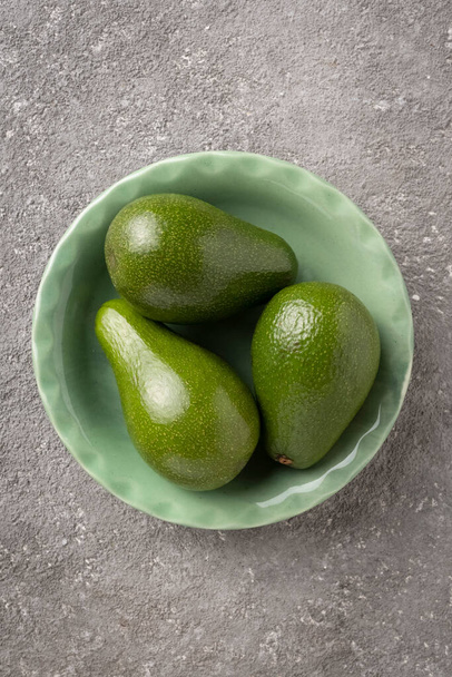 Three avocado fruits in a green plate on a gray table. Close-up, copy space for text - Foto, Bild