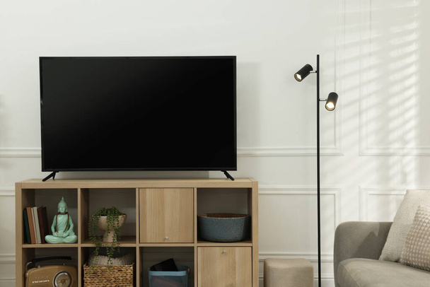 Μοντέρνα τηλεόραση στο ντουλάπι και λάμπα κοντά στο λευκό τοίχο σε εσωτερικούς χώρους. Εσωτερική διαρρύθμιση - Φωτογραφία, εικόνα