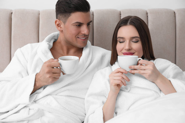 Happy couple in bathrobes with coffee on bed at home - Photo, image