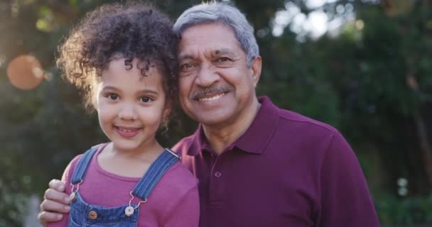 Faces of a grandfather and granddaughter smiling, bonding and hugging together in nature outside. Portrait of a little girl embracing, looking happy and spending quality time with her grandpa at park. - Filmagem, Vídeo