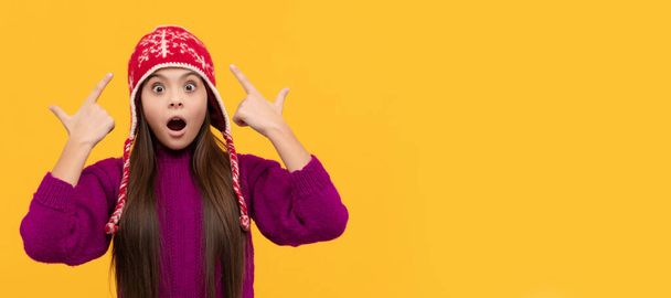 surprised kid in earflap hat on yellow background, keep warm. Child face, horizontal poster, teenager girl isolated portrait, banner with copy space - Photo, image