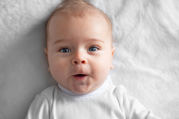 Ένα χαρούμενο αγοράκι, ένα μωρό, κείτεται πάνω σε μια λευκή κουβέρτα. Κοντινό πλάνο. - Φωτογραφία, εικόνα