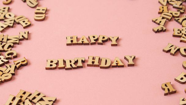 Слово "Happy Birthday", написанное на английском языке деревянными буквами на розовом фоне - Фото, изображение