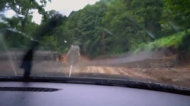 Car is moving along road washed out by rains, camera shoots inside from cabin. Mountain road of clay in rain. Impassable places. brushes clean window. Impassability. - Imágenes, Vídeo