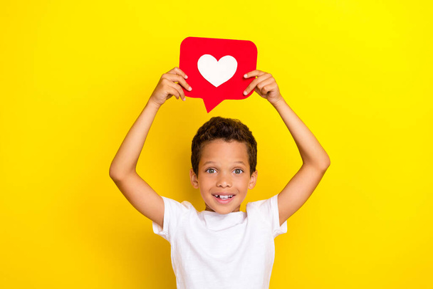 Photo of funny little boy hold heart wear white t-shirt isolated on yellow color background. - Foto, afbeelding