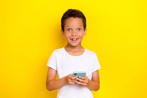 Photo of astonished satisfied cute stylish boy hand arm hold telephone impressed modern device isolated on yellow color background. - Foto, Imagem