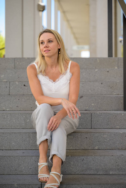 Pensive blond woman sitting on outdoor steps looking aside with an expression of longing - Fotoğraf, Görsel