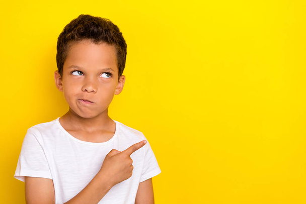 Photo of minded boy look advert banner offer arm demonstrates empty space dissatisfied shopping price isolated on yellow color background. - 写真・画像
