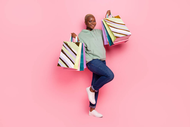 Full length image of cheerful young lady addicted to shopping raise up bags full of clothes isolated on pink color background. - Fotografie, Obrázek