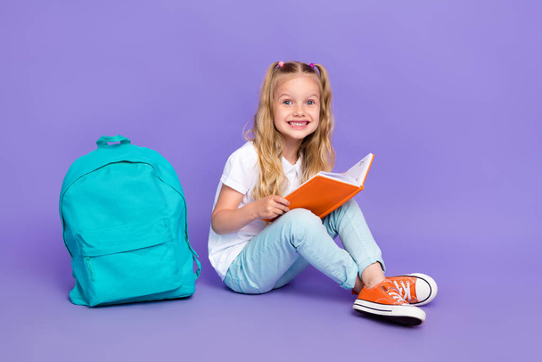 Full size photo of little girl ponytails toothy smile read textbook school bag wear trendy white outfit isolated on purple color background. - Fotografie, Obrázek