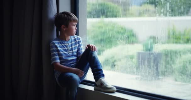 Sad, depressed and frustrated child with mental health problems watching the rain through a window at home. Abused, unhappy little boy looking lonely and upset, thinking of unhappy news of divorce. - Video