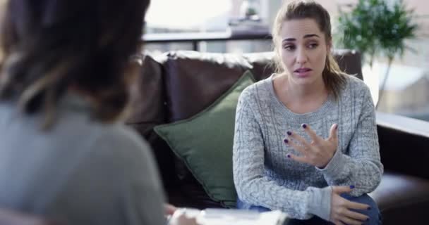 Frustrated young woman speaking to psychologist at therapy session, discussing mental health problems. Female patient feeling stress and anxiety, sitting on sofa in psychiatrist or doctor office - Filmagem, Vídeo