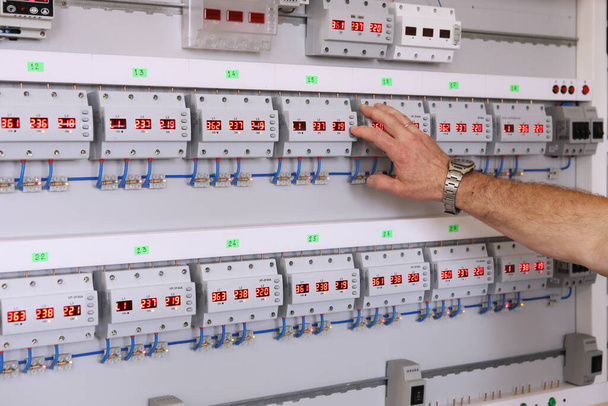 Service center for the repair of power voltage relays. Human checking electrical device with digital display. Numbers on the test bench. Manufacture of sockets volt control and quality control.. - Foto, imagen