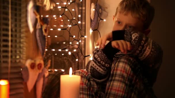 Fin de Navidad poco triste muchacho sentado en el alféizar de la ventana - Imágenes, Vídeo
