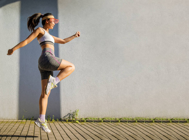 Молодая азиатка с правильным телом прыгает и бежит на сером фоне. Женская модель в спортивной одежде на открытом воздухе. - Фото, изображение