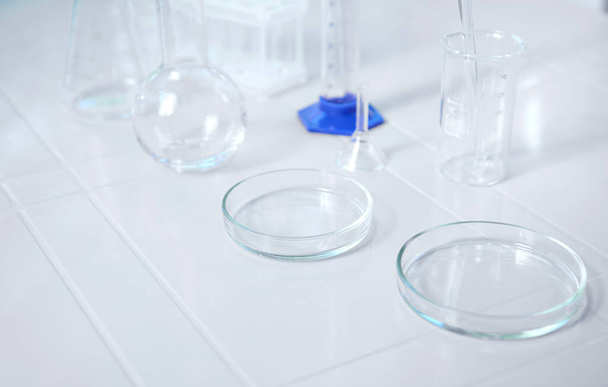 Glass lab dishes on white table on the background of labware such as beaker, flask, graduated cylinders, test tubes. Science chemistry. Scientific biological and chemical laboratory with copy ad space - Photo, Image