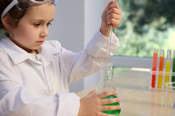 Close-up little girl chemist using a pipette, dripping some drops of liquid chemicals into a flask, concluding scientific experiment in the school scientific laboratory. Entertainments for smart kids - Fotoğraf, Görsel
