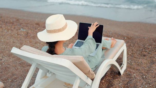 Rear view of freelancer woman working on laptop near the sea. Remote work concept. work on vacation. High quality 4k footage - Foto, immagini