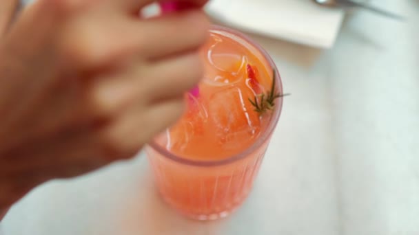Female hand stir an orange lemonade with ice in transparent glass. High quality 4k footage - Felvétel, videó